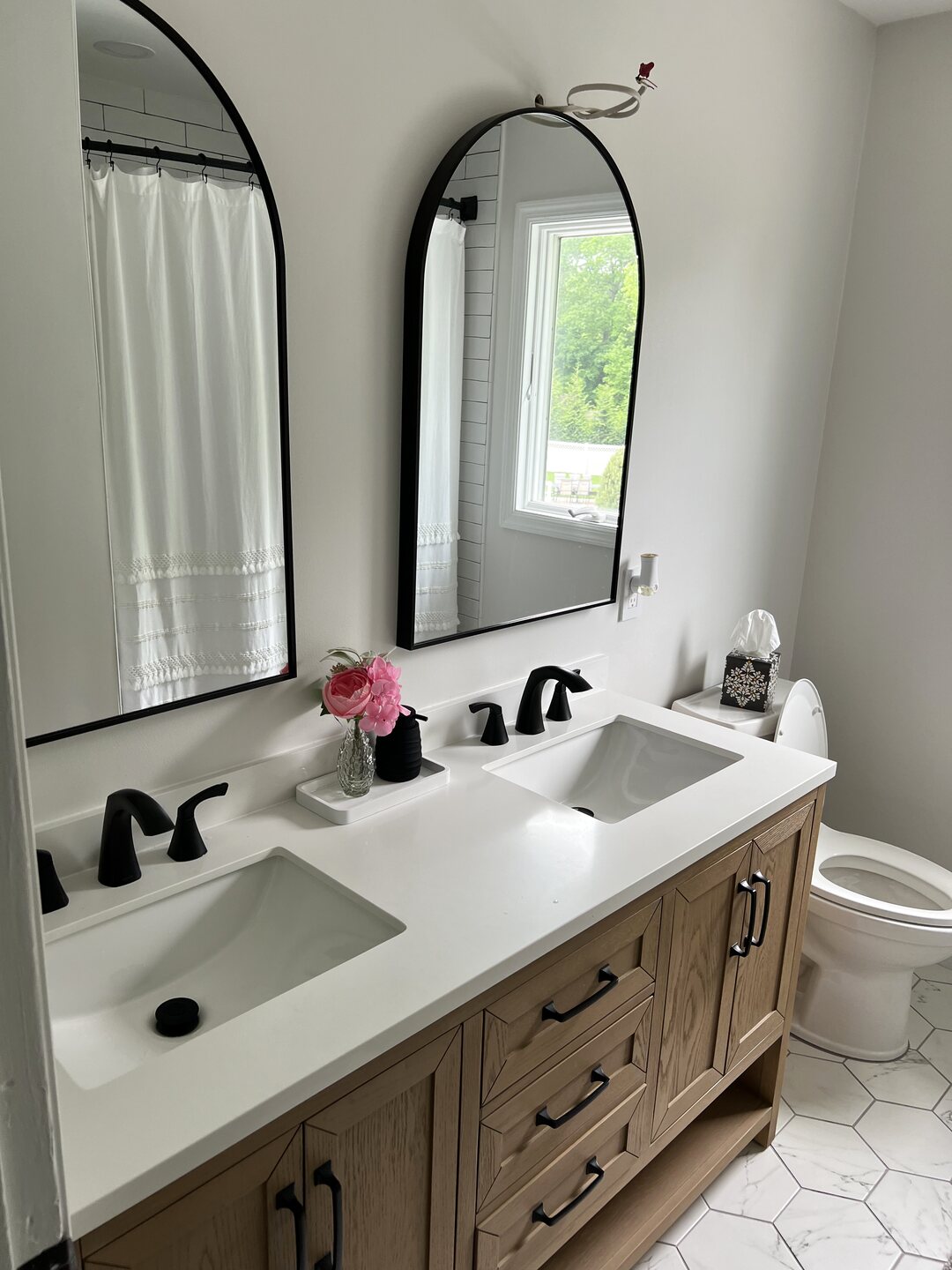 Finished bathroom remodel with a white oak double vanity, quartz countertop, matte black fixtures and arched black mirrors.