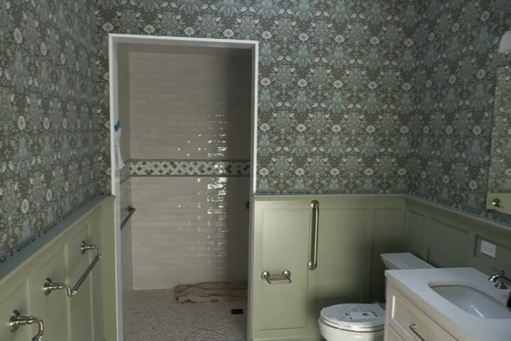 Bathroom with painted wainscot panelling, patterned wallpaper and a tiled shower entry.